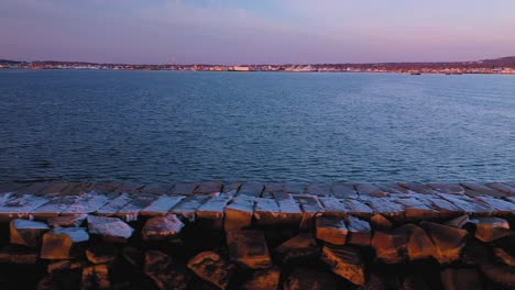 Close-aerial-slide-along-a-snow-dusted-rocky-breakwater-in-Rockland-Maine