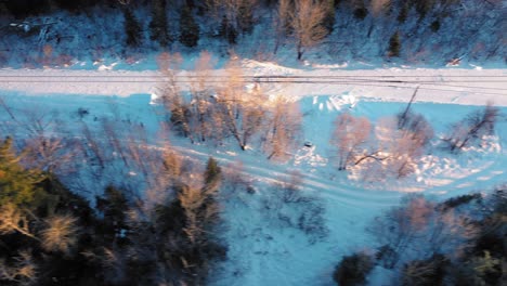 Aerial-TOP-DOWN-SLIDE-over-a-snow-covered-set-of-railroad-tracks-running-through-a-winter-forest
