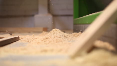 Close-up-view-of-sawdust-falling,-creating-a-pile-on-the-floor-in-the-workshop