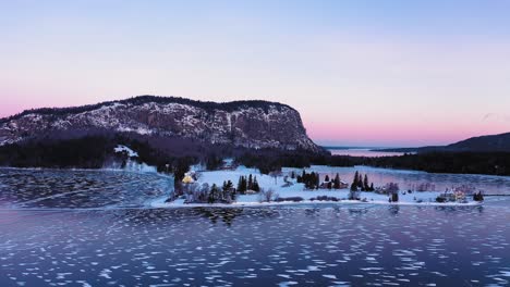 Orbiting-around-the-a-peninsula-in-a-frozen-lake-at-the-base-of-the-cliff-face-of-an-isolated-mountain-at-dawn-with-patterns-of-lines-and-circles-in-the-ice