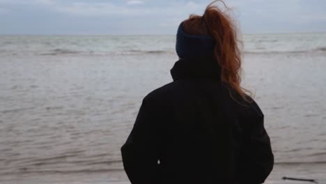 Traurige-Und-Melancholische-Strand--Und-Meereslandschaft-Mit-Einem-Mädchen-Mit-Schönen-Roten-Haaren,-Das-Es-An-Einem-Kalten-Und-Windigen-Wintertag-Beobachtet