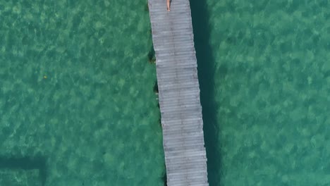 Aerial-of-a-girl-in-a-yellow-bikini-walking-alone-on-a-pier,-camera-down
