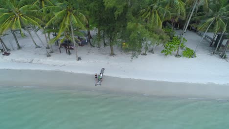 Aerial,-tracking,-drone-shot-people-enjoying-a-warm-day,-on-a-paradise-beach,-at-turquoise-sea,-,-on-a-sunny-day,-in-Koh-Kood,-Thailand,-Asia