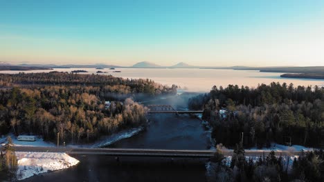 Aerial-footage-flying-towards-a-bridge-and-railroad-trestle-that-cross-over-the-outlet-of-a-frozen-lake