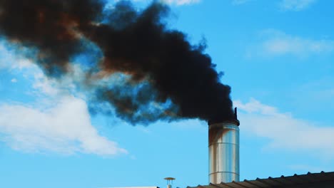 Thick-black-smoke-billowing-out-of-factory-smokestack,-blue-sky-background
