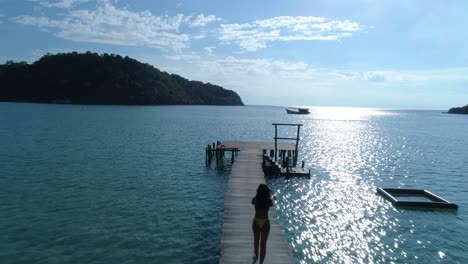 Fit-Asian-girl-walking-on-a-pier-in-the-ocean-on-a-tropical-island,-koh-kood,-thailand