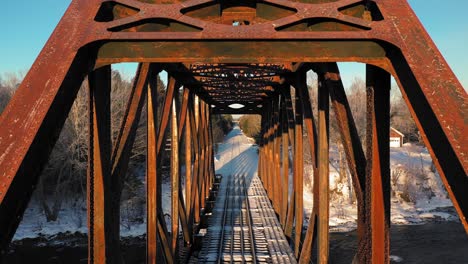 Aerial-CRANE-up-close-up-of-a-rusty-railroad-trestle-on-a-cold-winter-morning-revealing-a-truck-crossing-the-tracks-in-the-distance