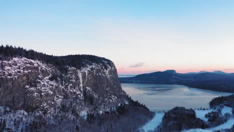 Aerial-view-looking-along-the-edge-of-a-cliff-during-a-winter-sunrise-while-flying-up-and-to-the-left