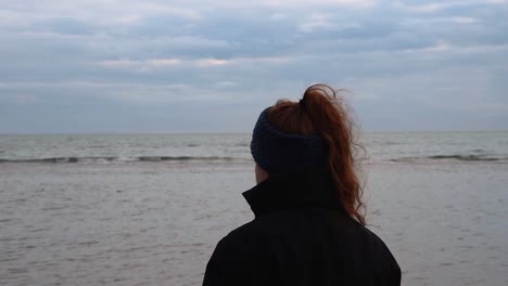 sad-and-melancholy-beach-and-sea-landscape-with-a-girl-with-beautiful-red-hair-watching-it-in-a-cold-and-windy-winter-day