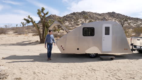 Slow-motion-shot-of-a-handsome-man-in-the-desert-on-a-camping-trip-in-a-metal-teardrop-travel-trailer-and-tiny-house
