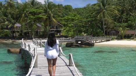 Asian-girl-in-a-white-dress-walking-over-a-wooden-bridge-on-a-tropical-island