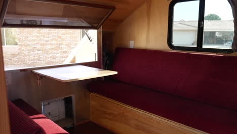 Reveal-shot-of-the-interior-of-a-deluxe-teardrop-travel-trailer-with-a-fold-out-table-and-windows-with-red-cushions-on-the-seats