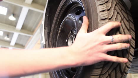 Close-up-of-a-male-mechanic-in-a-workshop-putting-back-a-car-wheel