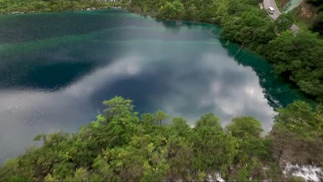 Reversal-drone-shot-over-dark-blue-water-and-past-a-tree-line-with-multiple-small-waterfalls