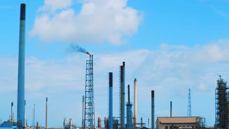 Slow-motion-wide-angle-shot-of-a-large-industrial-refinery-with-black,-polluting-smog-pouring-out-into-a-clear-blue-sky-in-Curacao