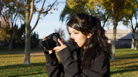 A-beautiful-woman-model-taking-pictures-with-a-professional-digital-mirrorless-camera-during-a-photo-shoot-in-a-park-during-autumn