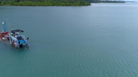 Half-sunken-fishing-boat-on-the-shore-of-a-deserted-island-Sideways-drone-shot-Cropped