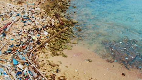 Pan-of-trash-and-litter-pollution-strewn-across-beach-alcove,-Curacao,-Caribbean