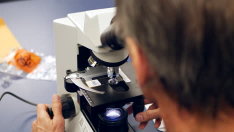 A-scientist-examining-a-slide-with-human-cancer-cells-through-a-microscope-in-a-medical-research-laboratory