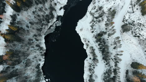 Aerial,-birdseye,-top-down,-drone-shot,-above-a-river,-surrounded-by-leafless-forest-and-first-snow-on-the-ground,-near-Joensuu,-North-Karelia,-Finland