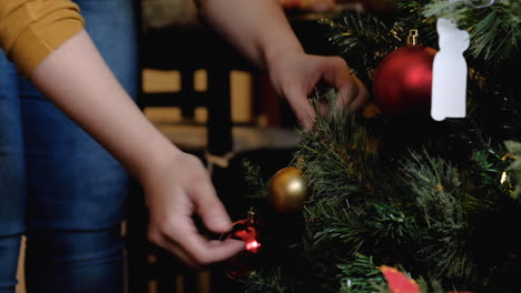 Woman-hands-placing-yellow-ball-ornament-setting-up-christmas-tree-with-lights-tight-shot