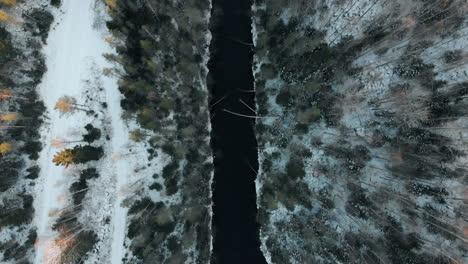 Aerial,-birdseye,-top-down,-drone-shot,-above-a-river,-surrounded-by-leafless-trees-and-first-snow-on-the-ground,-on-a-cloudy,-autumn-day,-near-Joensuu,-North-Karelia,-Finland