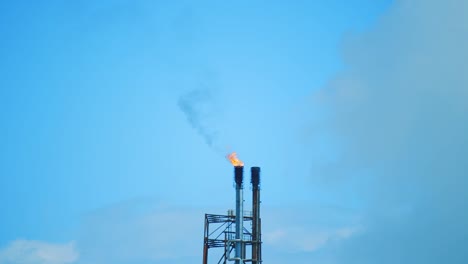 Slow-motion-shot-of-the-top-of-an-industrial-refinery,-centrally-framed,-showing-black-polluting-smog-being-emitted-into-a-clear-blue-sky-in-Curacao