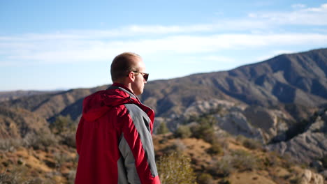A-young-man-in-a-red-jacket-camping-in-the-California-mountains-on-the-edge-of-a-cliff-celebrating-reaching-his-goal