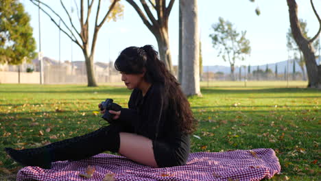 A-beautiful-girl-photographer-looking-at-photos-on-her-professional-mirrorless-digital-camera-on-a-blanket-in-the-park