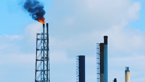 Zeitlupenaufnahme-Von-Feuer-Und-Schwarzem,-Umweltschädlichem-Smog,-Der-Von-Der-Spitze-Einer-Industriellen-Raffinerie-In-Einen-Klaren-Blauen-Himmel-In-Curacao-Strömt