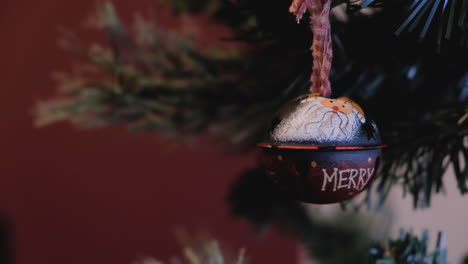 Red-santa-claus-with-merry-inscription-christmas-ornament-hanging-from-tree-detailed-shot-blurried-red-background