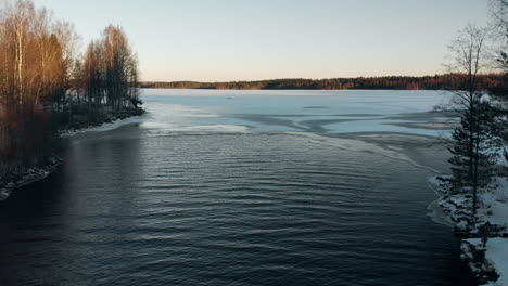 Antenne,-Rückwärtsfahrt,-Drohnenschuss,-über-Einem-Fluss,-Vom-Ersten-Eis-Auf-Einem-See,-Umgeben-Von-Blattlosem-Wald-Und-Frühem-Schnee-Auf-Dem-Boden,-An-Einem-Sonnigen-Herbsttag,-In-Der-Nähe-Von-Joensuu,-Nordkarelien,-Finnland