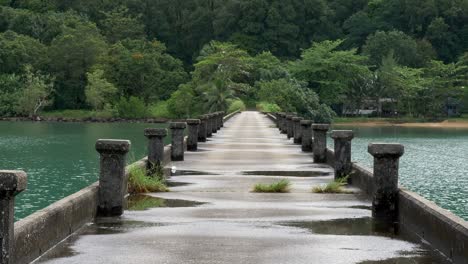 Static-shot-of-a-concrete-pier-in-the-ocean-after-rainfall-with-green-lush-forest-in-the-back-Cropped