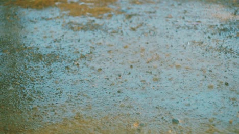 Close-up-slow-motion-shot-of-rain-drops-falling-on-a-muddy,-dirty-road-in-Curacao