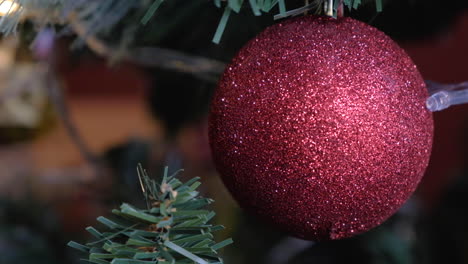 Shining-red-christmas-ball-ornament-placed-on-tree-with-blurred-lights-background