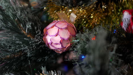 Red-Christmas-floral-bauble-hanging-in-a-Christmas-tree-with-a-hand-made-Santa-out-of-focus-in-the-background