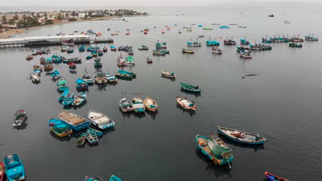 Pan-right-aerial-shot-of-Paracas-town-Marina,-with-fishing-boats-and-seabirds