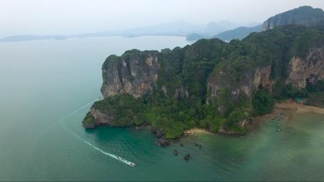 Stellar-aerial-shot-over-limestone-cliffs-on-a-mountainous-tropical-island-while-speedboats-zip-through-the-waters-below
