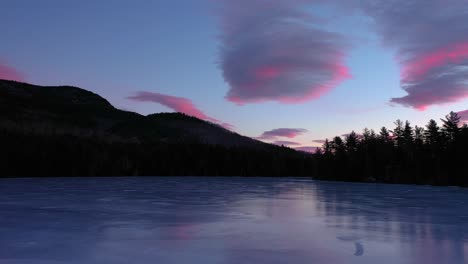 Aerial-footage-flying-low-across-the-surface-of-a-frozen-pond-towards-pink-and-blue-cotton-candy-clouds