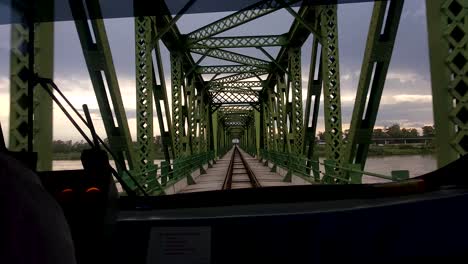 POV-view-over-train-drivers-shoulder-watching-out-of-front-train-window-as-it-crosses-green-metal-bridge-structure