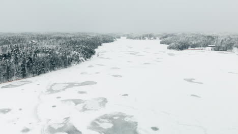 Antenne,-Tracking,-Drohnenschuss,-über-Schwachem,-Schneebedecktem-Eis,-Auf-Nuuksion-Pitkajarvi,-Umgeben-Von-Winterwald,-An-Einem-Bewölkten-Tag,-Im-Nuuksio-Nationalpark,-In-Espoo,-Uusimaa,-Finnland