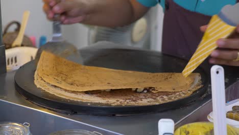 Slow-motion:-Chef-finishing-up-pancake,-folding-it-up-and-putting-it-into-the-holder,-Dream-World,-Thailand