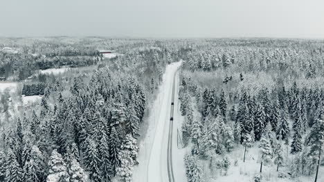 Aerial,-drone-shot,-following-cars,-driving-on-a-slippy-road,-between-snow,-covered-trees-and-winter-forest,-on-a-overcast-day,-near-Nuuksio-national-park,-in-Espoo,-Uusimaa,-Finland