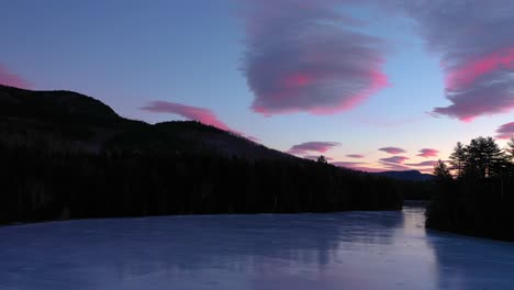 Aerial-footage-rising-up-above-the-surface-of-a-frozen-pond-flying-towards-pink-and-purple-cotton-candy-clouds