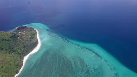 Panning-aerial-shot-from-turquoise-and-navy-blue-coloured-water-to-a-mountainous-tropical-island