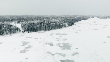 Aerial,-drone-shot,-over-weak,-snow-covered-ice,-on-Nuuksion-Pitkajarvi,-towards-winter-forest,-on-a-overcast-day,-in-Nuuksio-national-park,-in-Espoo,-Uusimaa,-Finland