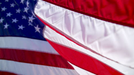 Nahaufnahme-Einer-US-Flagge,-Die-An-Einem-Sonnigen-Tag-In-Zeitlupe-Draußen-Weht,-Mit-Einem-Verschwommenen-Hintergrund-Des-Desserts