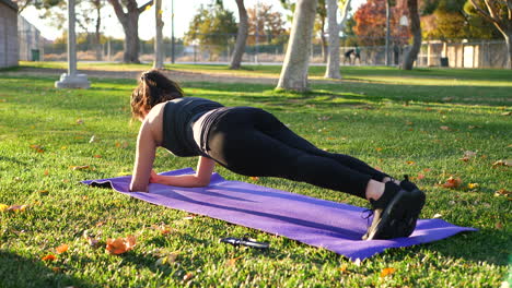 Eine-Junge-Frau,-Die-In-Zeitlupe-In-Einem-Park-Auf-Einer-Yogamatte-Eine-Planke-Macht-Und-Ihre-Bauch--Und-Rumpfmuskulatur-Trainiert
