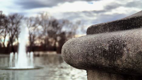 Close-up-footage-of-a-unique-concrete-post-in-front-of-a-scenic-pond-and-flowing-fountain-at-an-outdoor-park