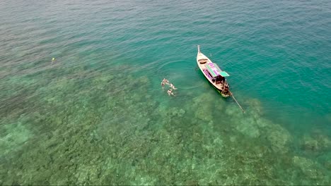 Divertida-Toma-Aérea-De-Un-Grupo-De-Turistas-Nadando-Junto-A-Un-Barco-Tradicional-Tailandés-Y-Luego-Saludan-A-La-Cámara